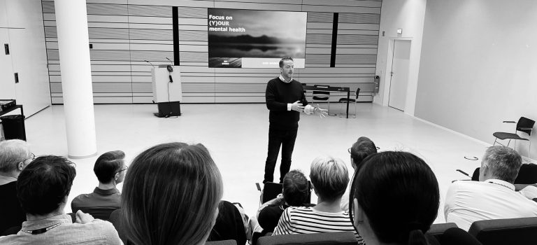 Bjorn Kiggen als Speaker auf einer großen Leinwand während eines hybriden Events zu mentaler Gesundheit.