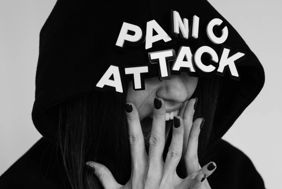 Schwarz-Weiß-Foto einer schreienden Person mit einer schwarzen Kapuze, über deren Augen die Worte 'PANIC ATTACK' als 3D-Buchstaben prangen – eine dramatische Visualisierung einer Panikattacke und eines Angstzustands.