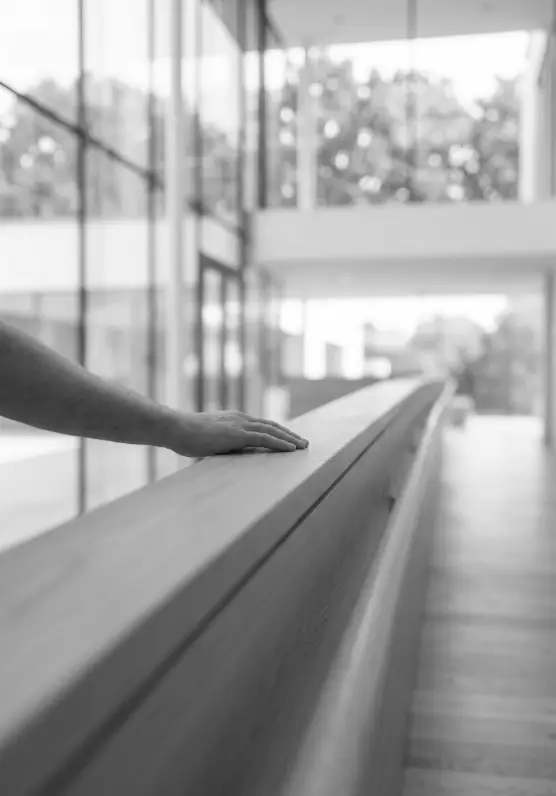 Nahaufnahme einer Hand, die ruhig über ein stabiles Holzgeländer streicht. Der helle, offene Hintergrund symbolisiert Sicherheit und klare Leitplanken im Unternehmen.